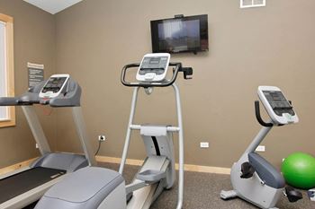 A gym with treadmills, exercise bike and a television mounted on the wall.